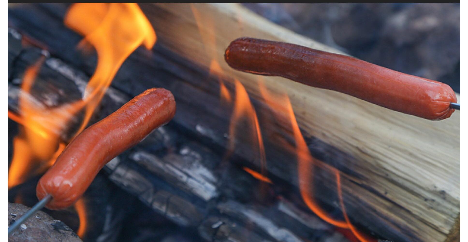 Hot dogs roasting over a campfire.